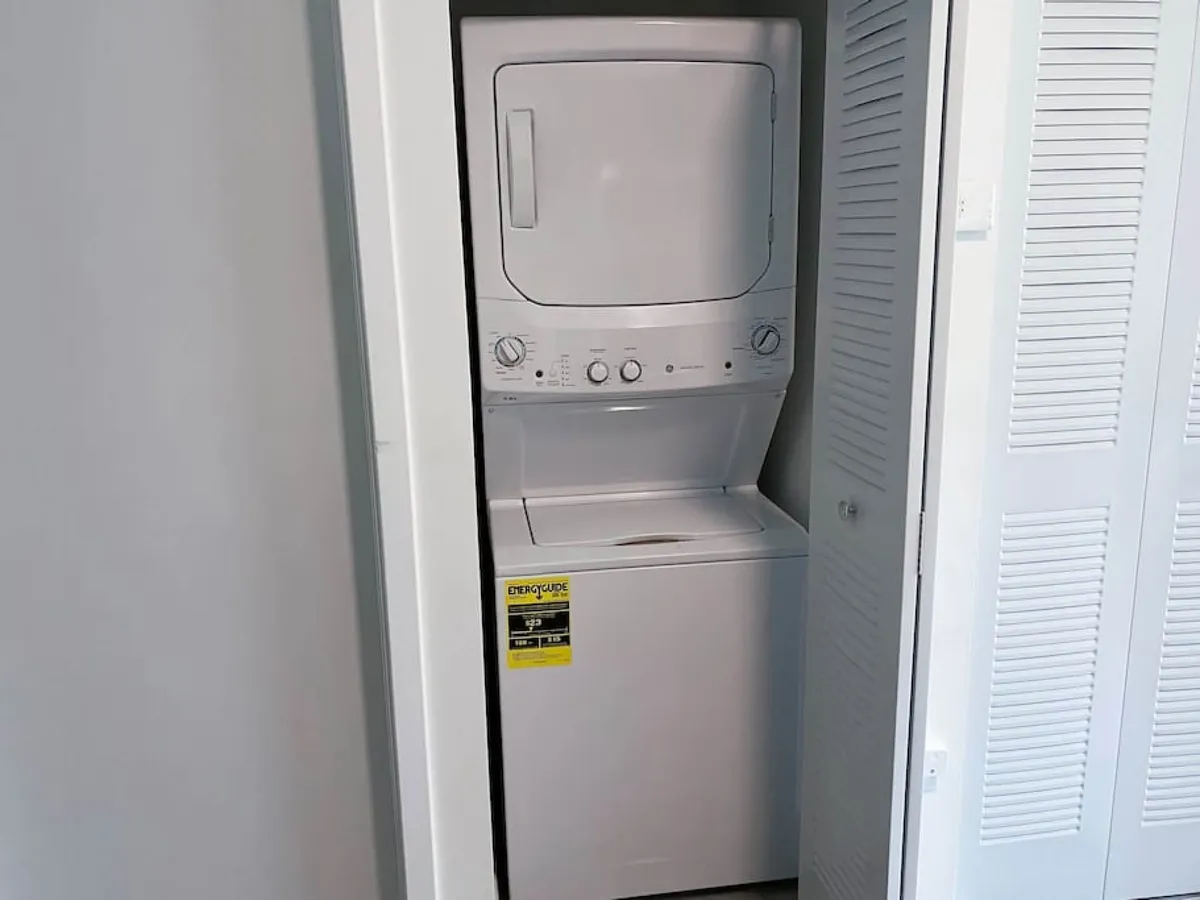 This image shows a stacked washer and dryer set within crisp white cabinetry, representing the apartment’s practical and efficient amenities adjacent to commonly accessed areas.