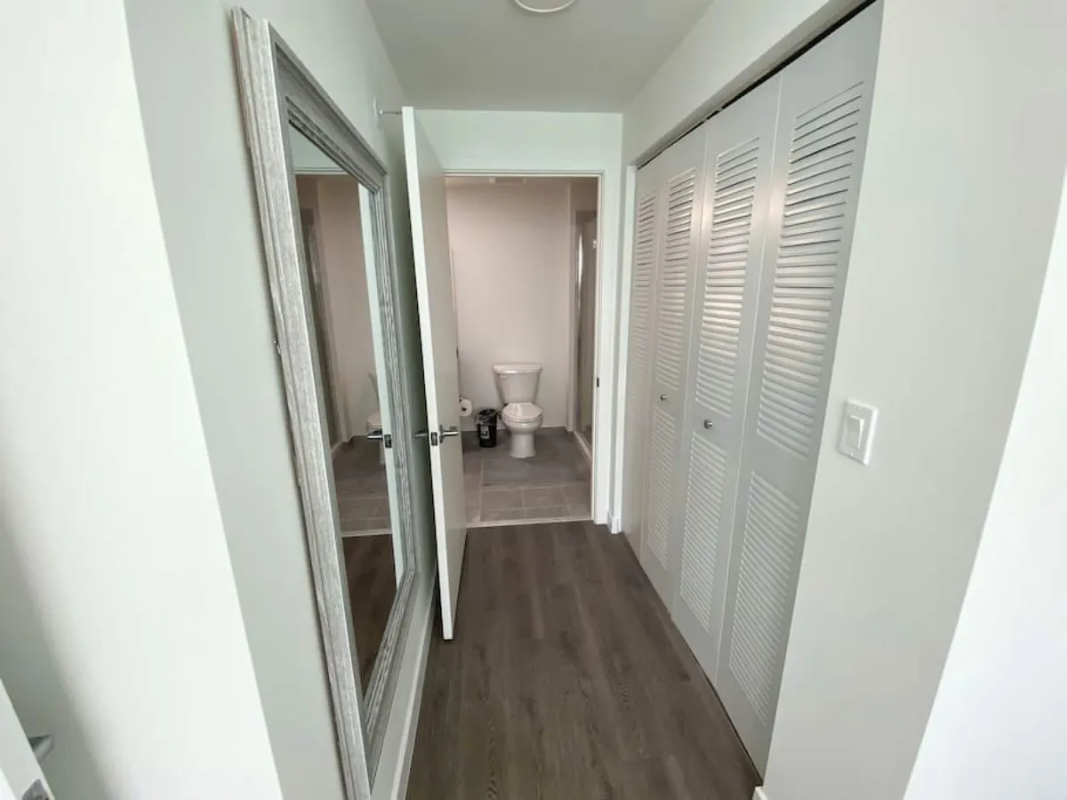 A functional area featuring a full-length mirror on the left, a clean bathroom visible through an open door, and white louvered closet doors on the right. The layout is wide and uncluttered, conducive to easy movement and accessibility for guests with mobility needs.